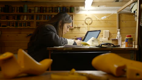 Mujer-Artesana-Dibujando-Obras-De-Arte-De-Diseño-De-Zapatos-Bajo-El-Foco-En-Un-Taller-De-Paneles-De-Madera