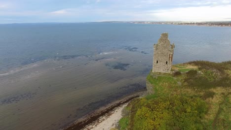 video aéreo de una torre de piedra en ruinas al borde de un acantilado sobre el agua y el horizonte en el fondo