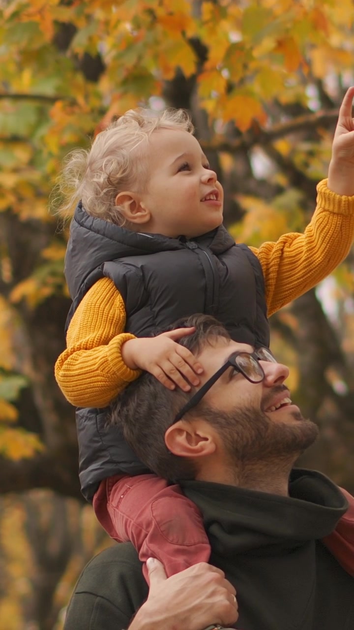 Padre che porta il bambino piccolo sulle spalle in un parco autunnale