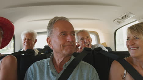 group of senior friends sitting in back of people carrier being driven to vacation