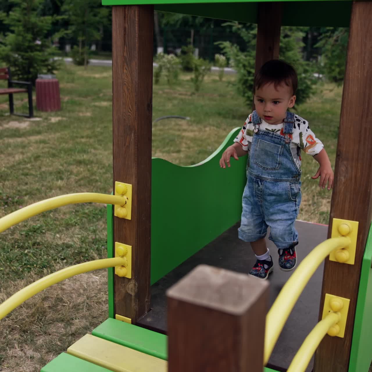 Caucasian toddler boy runs by the wooden bridge on the playground. Little boy spending time outdoors in summer