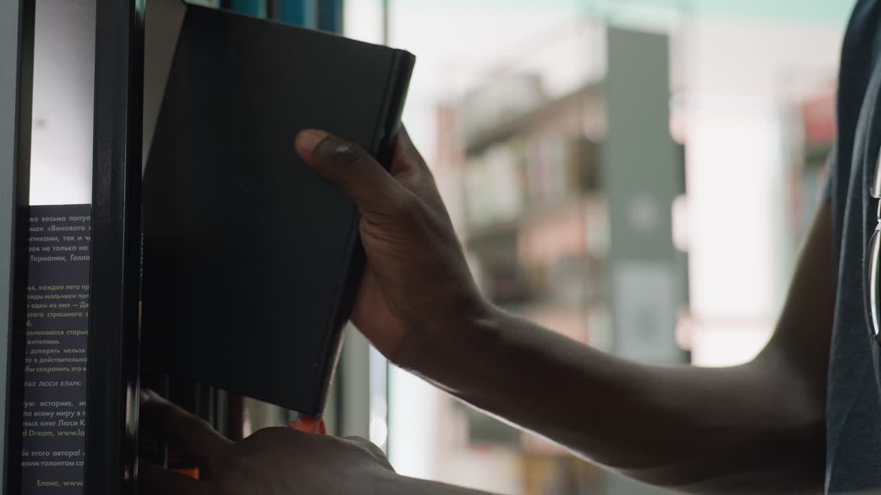 Close up of person returning book to shelf in library, with sunlight streaming in and blurred background of bookshelves creating peaceful academic atmosphere in quiet study environment