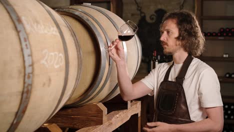 authentic shot of successful male sommelier is tasting a flavor and checking white wine quality poured in transparent glass in a wine cellar.