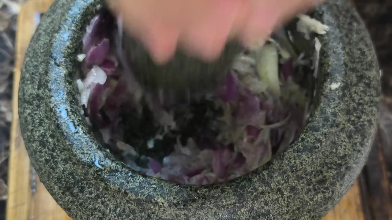 Cipolle e acciughe vengono pestate insieme usando un tradizionale mortaio e pestello di pietra. Questo metodo autentico prepara ingredienti saporiti per la cucina. Cattura una classica tecnica culinaria.