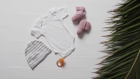 Video-of-white-baby-grow,-hat,-dummy-and-pink-booties-with-copy-space-on-white-background