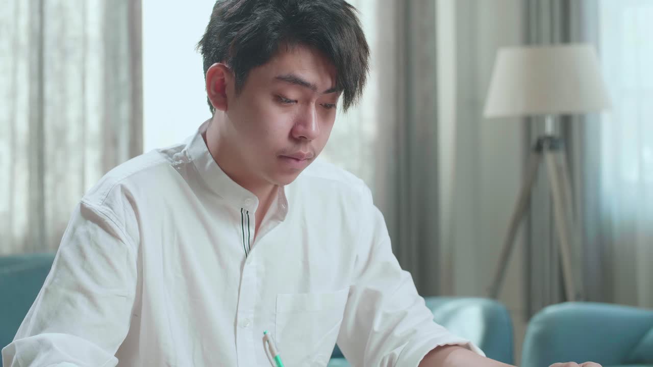 Close Up Of Asian Man Student Being Sleepy While Writing In The Notebook On The Table At Home