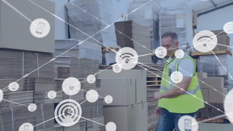 animación de una red de iconos digitales contra un trabajador caucásico apilando cajas en un almacén