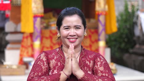 attractive asian woman in red lace dress folds hands and bows toward camera