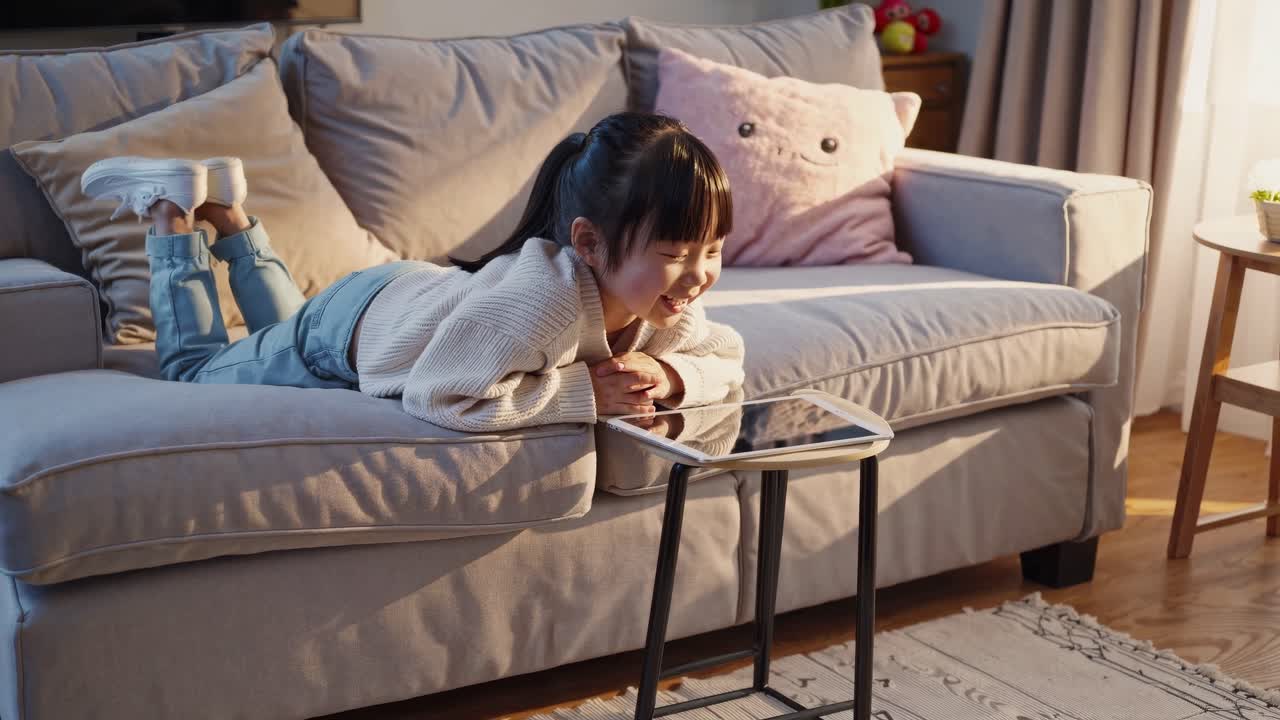 A cozy video scene of a child lying on a sofa, smiling at a tablet