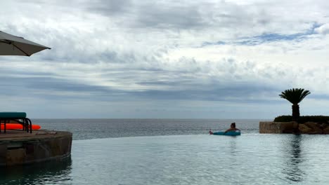 Lonely-Female-on-float-in-Infinity-Pool-of-Luxury-Hotel-Looking-on-Horizon