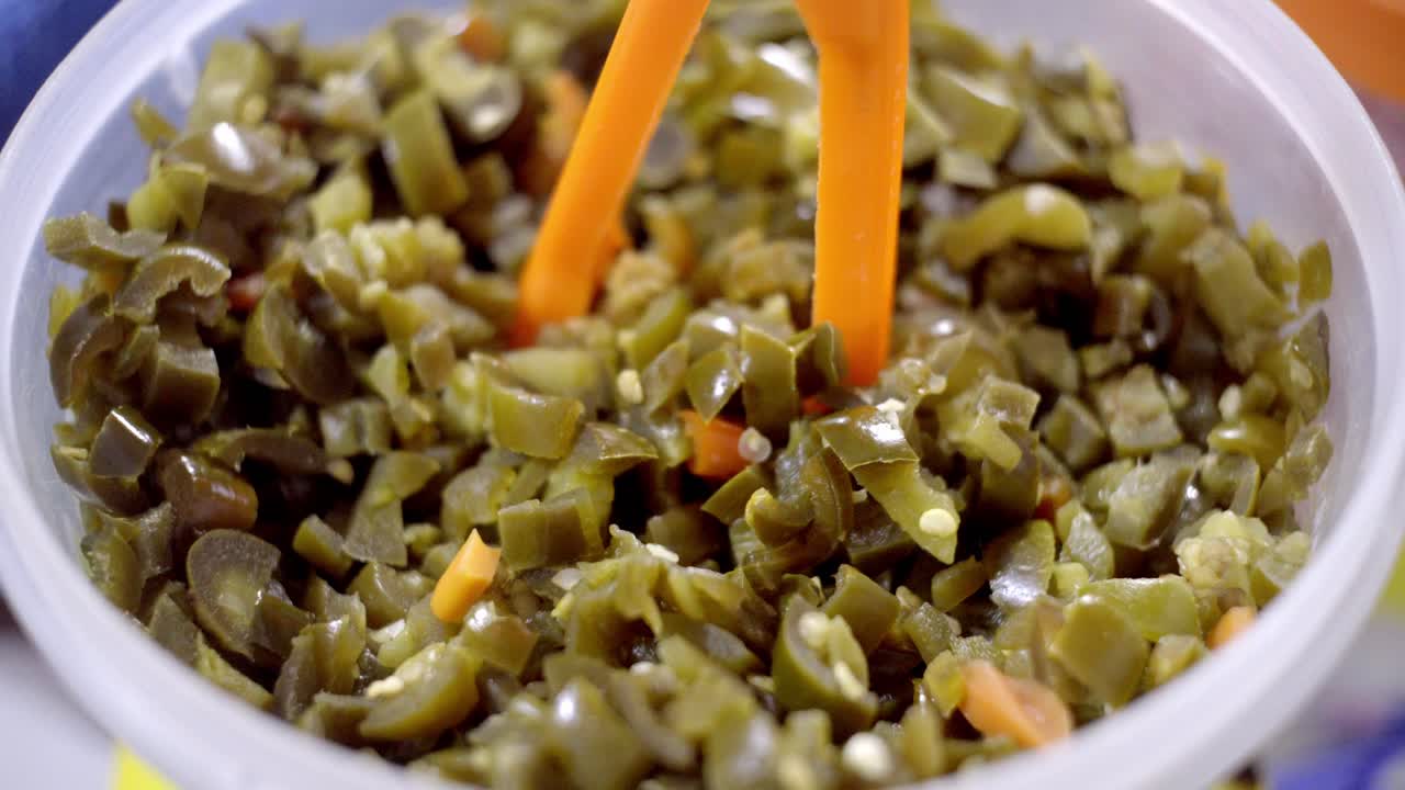 Primo piano sottile e a mano libera di verdure verdi sottaceto tritate servite in un contenitore di plastica, comune condimento da street food.