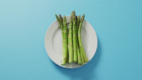 video of fresh asparagus on white plate over blue background