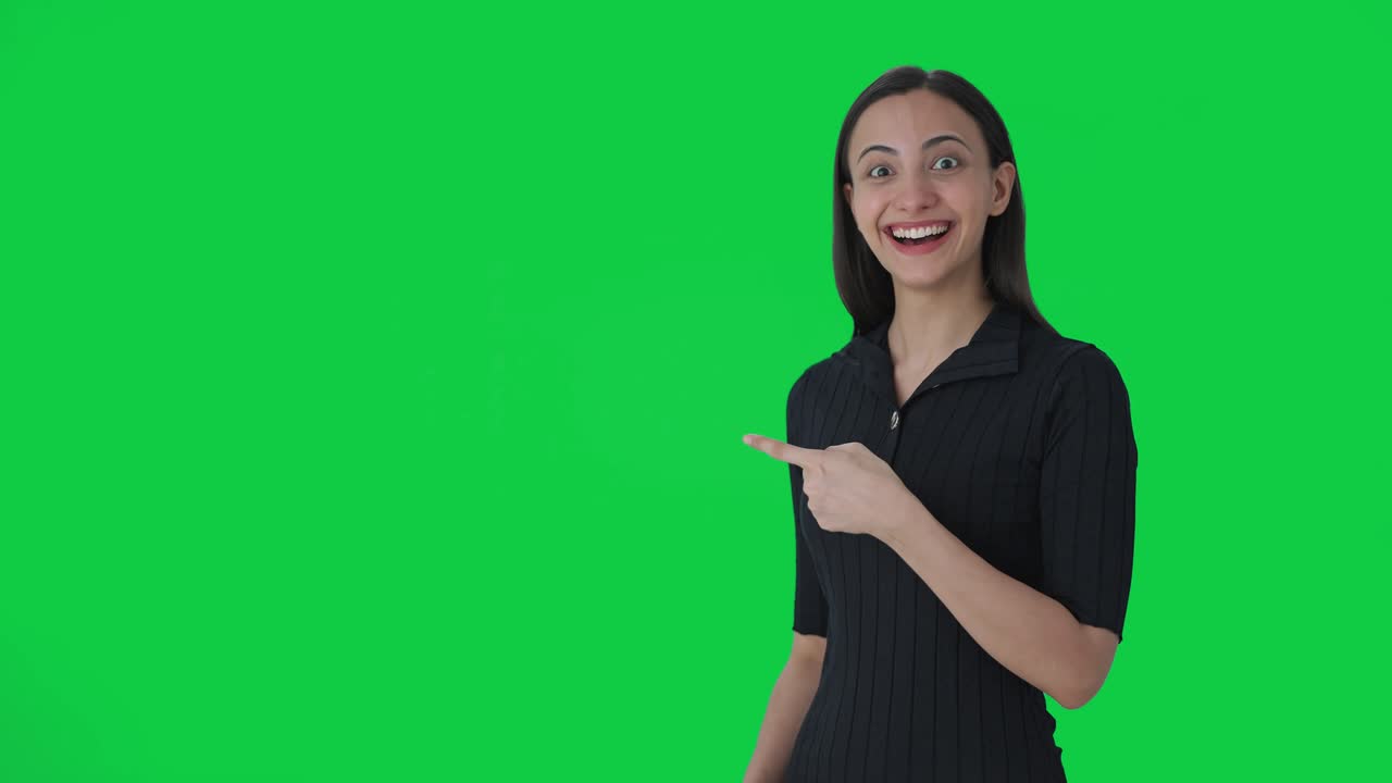 feliz presentadora de noticias india apuntando a la pantalla verde y mostrando los pulgares hacia arriba