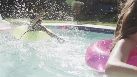 two happy diverse teenage female friends playing with inflatables in swimming pool in slow motion