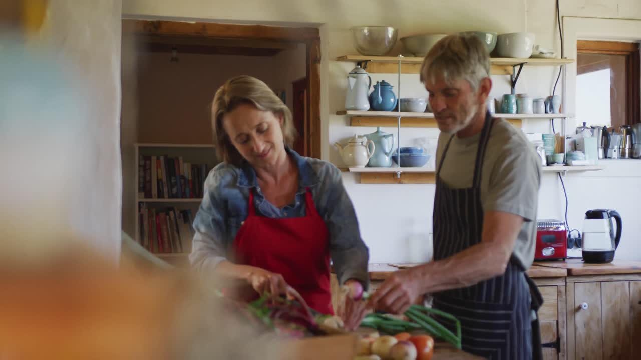 pareja caucásica mayor sonriente usando delantales y cocinando en la cocina