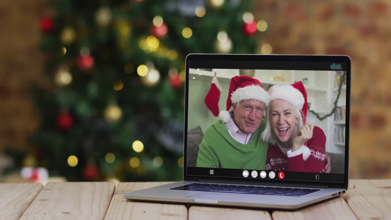 una pareja de alto nivel caucásica saludando en una videollamada en una computadora portátil, con un árbol de navidad