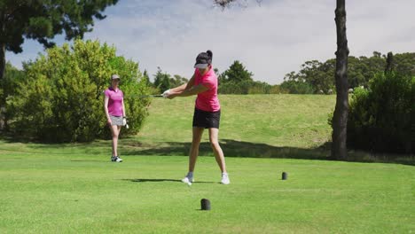 Two-caucasian-women-playing-golf-one-taking-shot-from-bunker