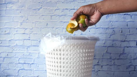 person throwing away orange peels in a trash can