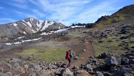 A-woman-with-a-backpack-walking-on-a-nice-sunny-day-on-a-mountain-trail-in-a-geothermal-area-in-Landmannalaugar-rainbow-mountains-in-Iceland