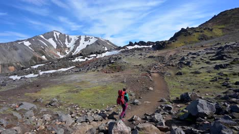 a woman with a backpack walking on a nice sunny day on a mountain trail in a geothermal area in landmannalaugar rainbow mountains in iceland