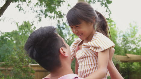 excited asian daughter running across garden at home and being lifted up by father