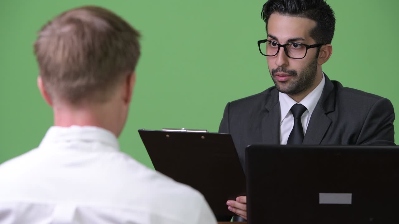 Two young multi-ethnic businessmen working together against green background