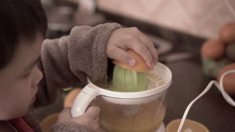 push in shot of a kid squeezing oranges and making orange juice with an electric squeezer