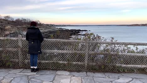 back view of lonely female standing by fence on viewpoint at gulf of maine, usa