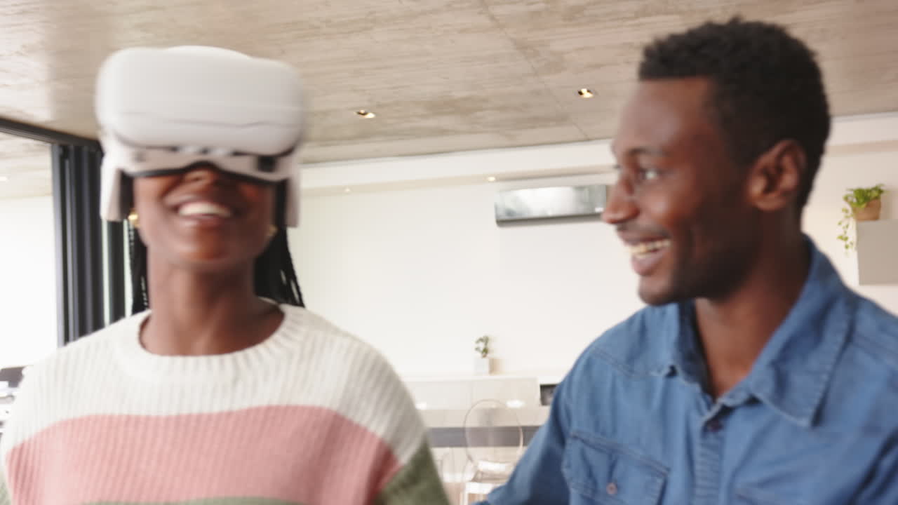 Using VR headset, woman smiling while man watching and laughing at home