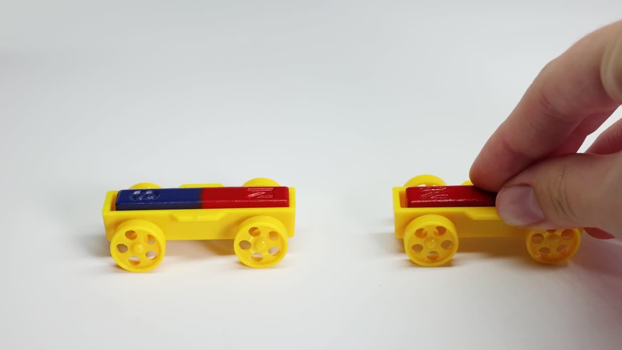 Hands manipulate magnetic toy cars on a white surface, illustrating magnetic attraction and repulsion with colorful blocks