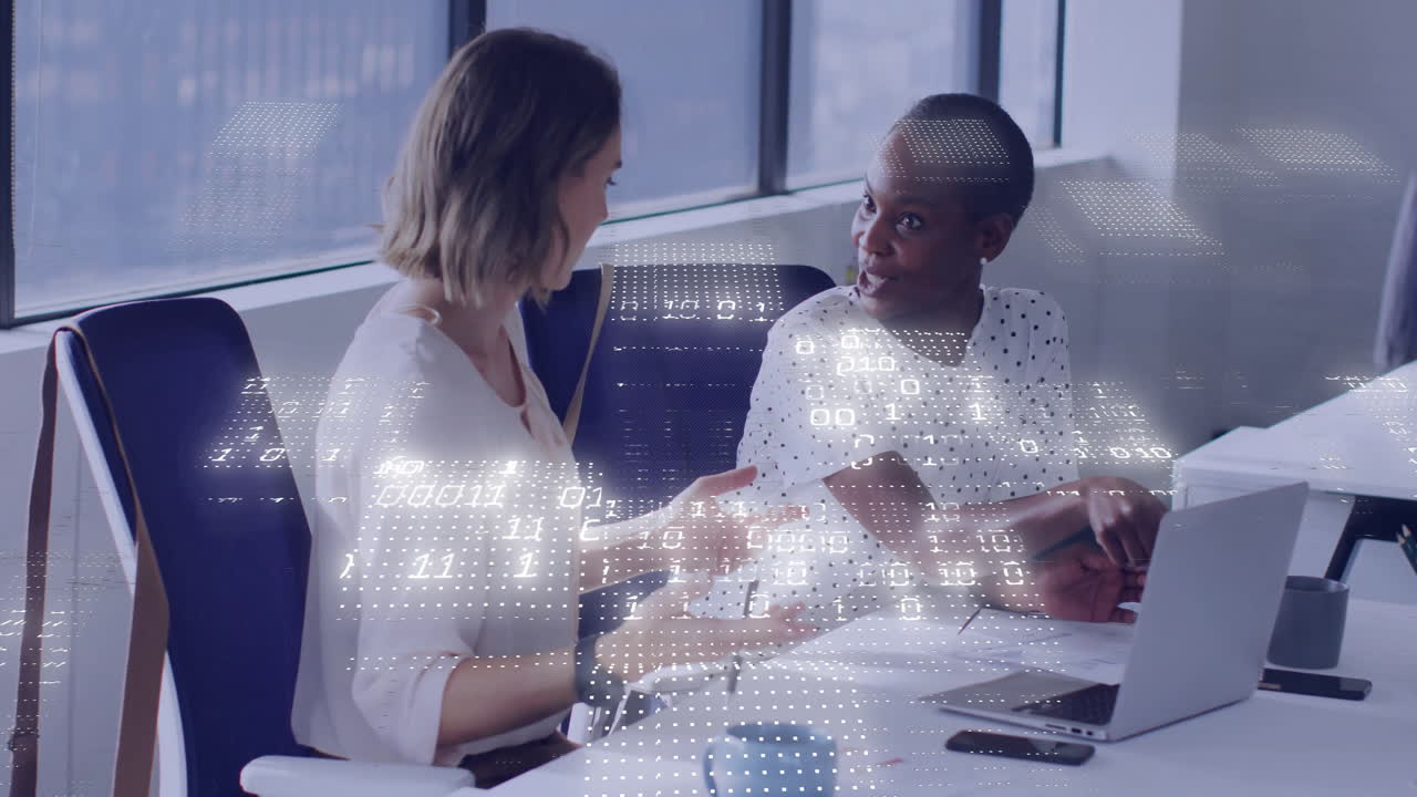 Två kvinnor diskuterar affärsstrategi vid ett modernt kontorsbord, med animerade datadiagram som svävar