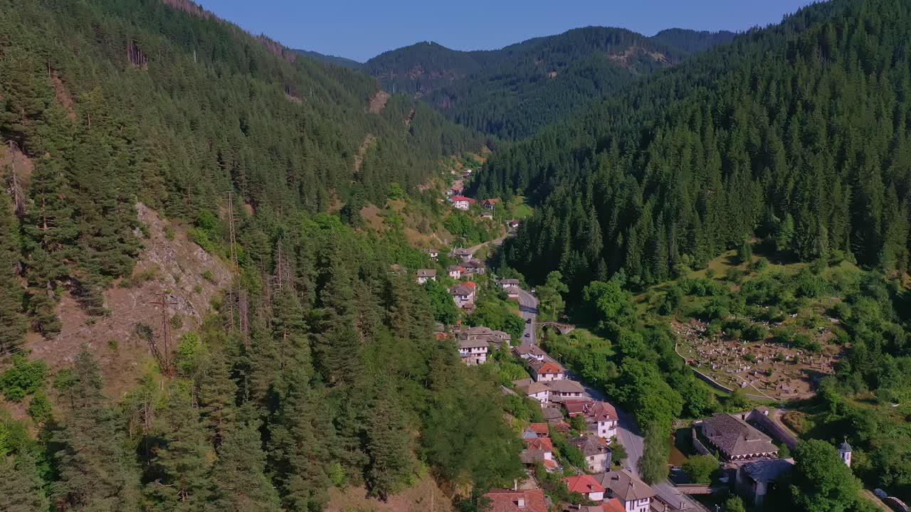 volando hacia atrás sobre un pequeño pueblo en las montañas rodeado de verdes colinas y árboles