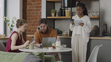 tres compañeros de cuarto desayunando y revisando notas en la computadora y el cuaderno en casa