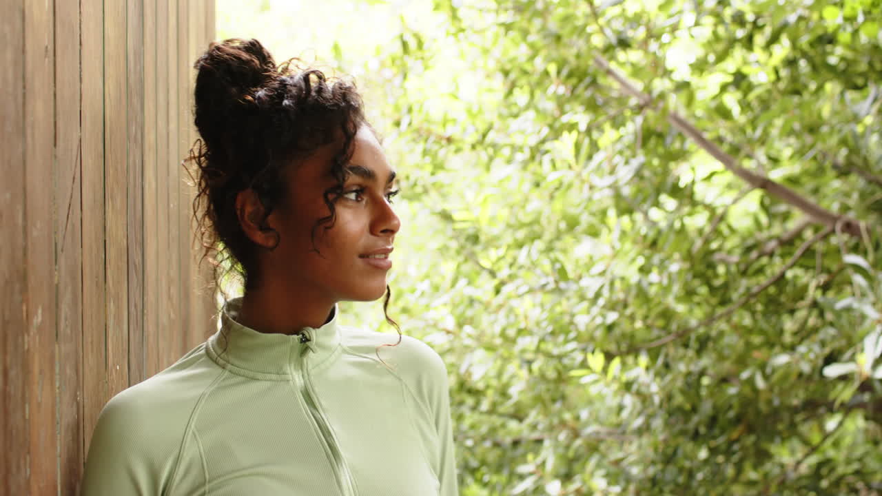 Smiling woman in green jacket enjoying nature on porch, looking content, copy space