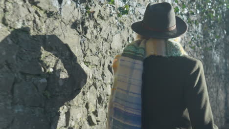 walking woman's shadow on stone wall adjusting her hat