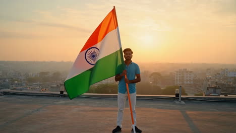 man proudly holding the indian flag on a rooftop at sunset
