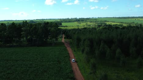 High-angle-aerial-view-of-vehicle-driving-on-a-dirt-road-on-his-way-to-the-farm-plantations-in-the-distance