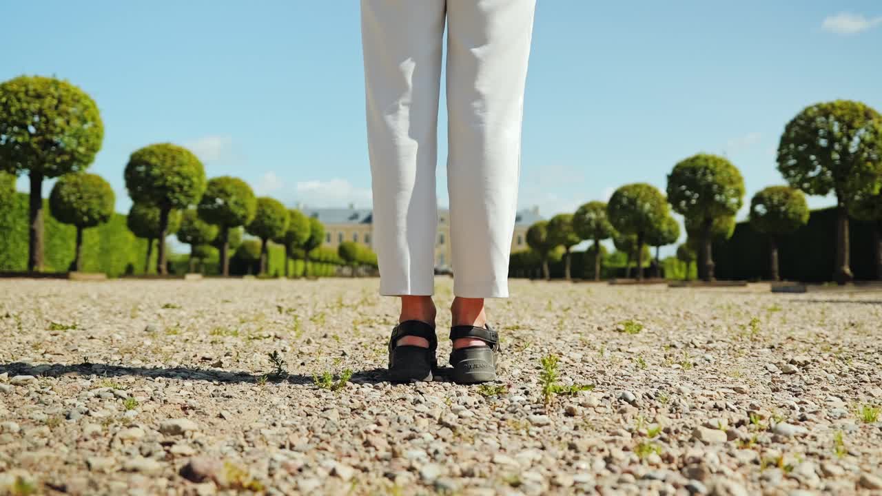 Sunny slow motion shot shows woman motionless in garden before palace
