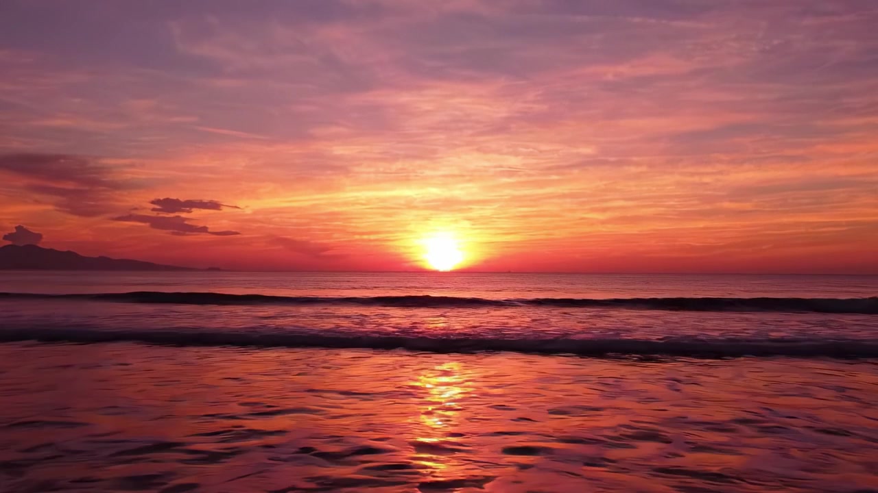 A mesmerizing sunset casts vibrant hues of orange, pink, and purple across a tranquil sea, reflecting stunning colors and creating a serene atmosphere at the edge of the horizon.