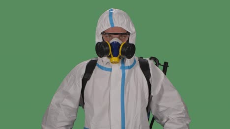 portrait male in a protective suit, safety glasses, gloves and a respirator looks confidently into the camera and then folds his arms in front of him. green screen, chroma key. slow motion. close up