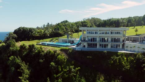 Cinematic-panning-FPV-drone-shot-of-a-luxurious-private-resort-on-the-side-of-an-island-surrounded-by-lush-green-foliage