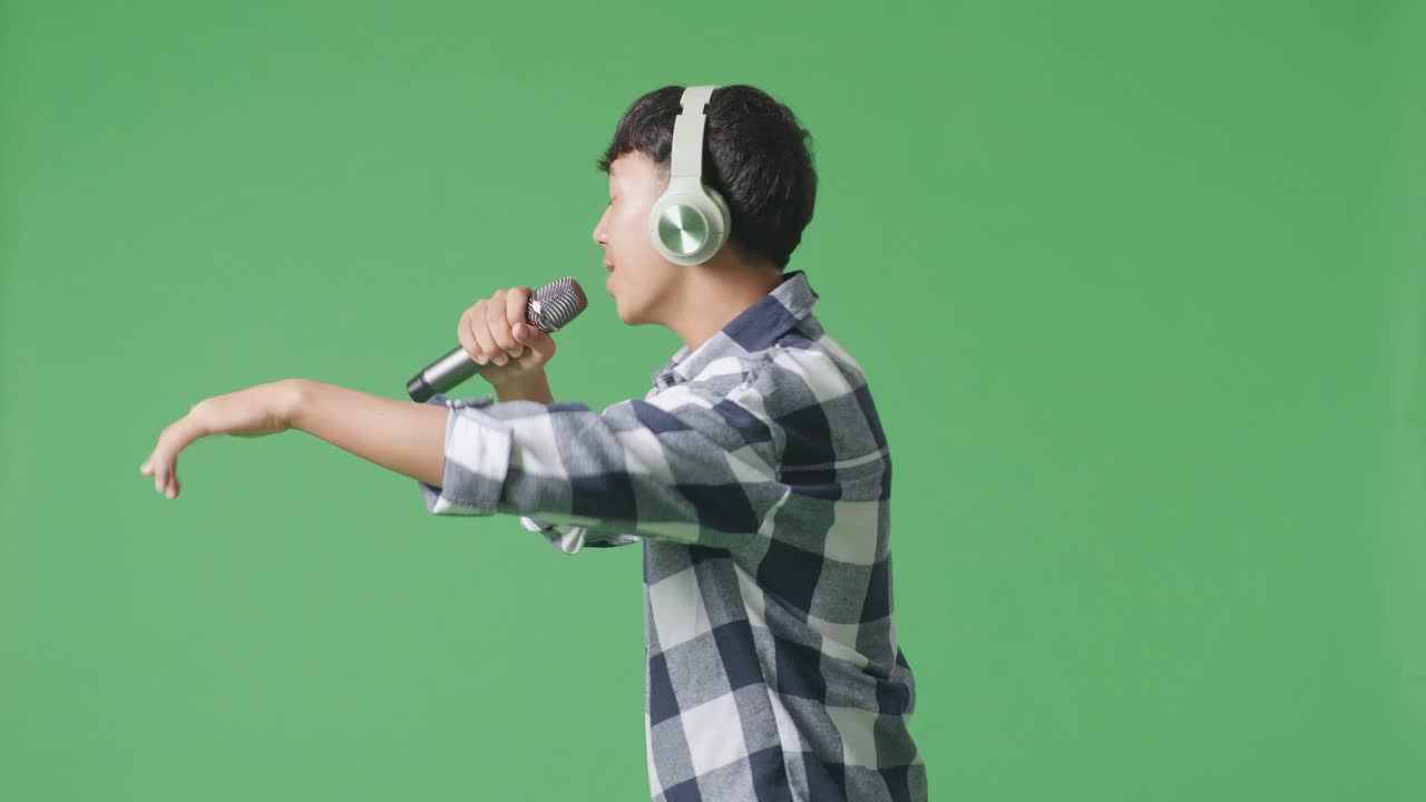 녹색 스크린 배경에서 마이크를 들고 하는 젊은 아시아 십대 소년의 측면 시각