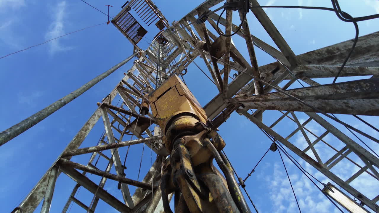 Drilling equipment hanging on the thick metal wires vibrating from work. Low angle view on the derrick for oil production.