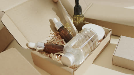 close up of cardboard boxes with glass bottles, cream tub and toothbrush on beige background