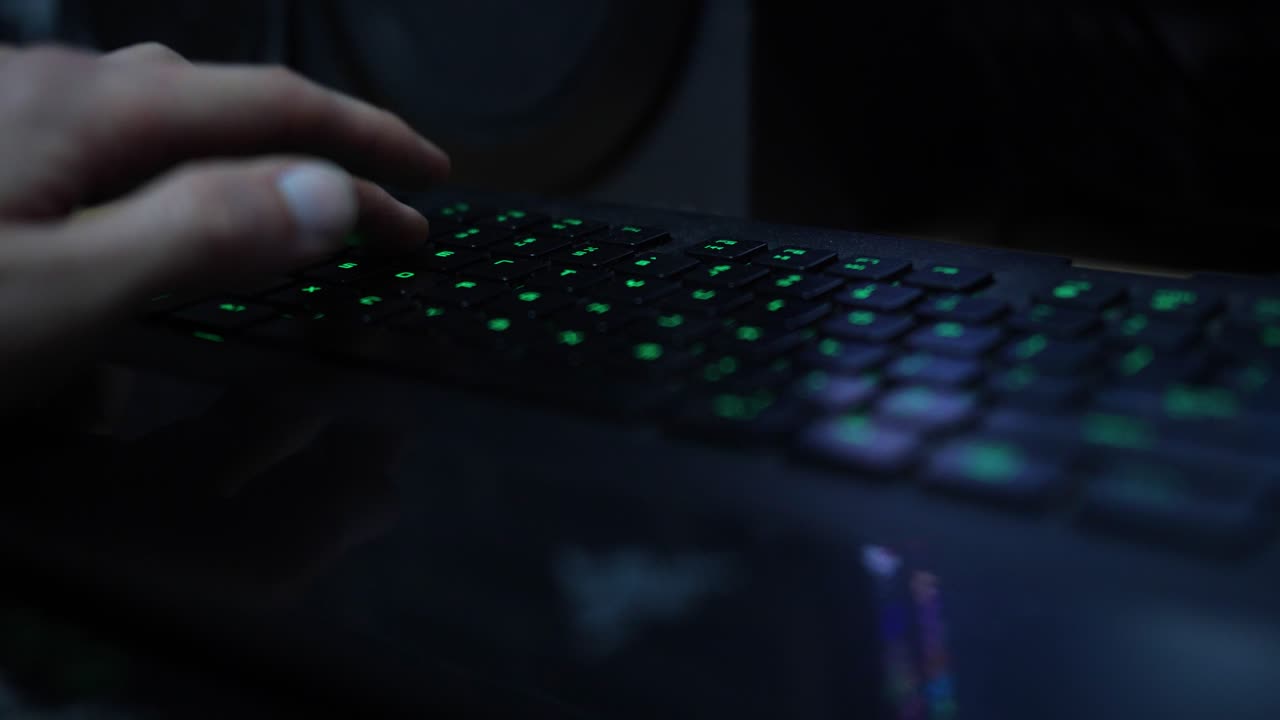 Light skin hand typing keystrokes into mechanical keyboard, green light