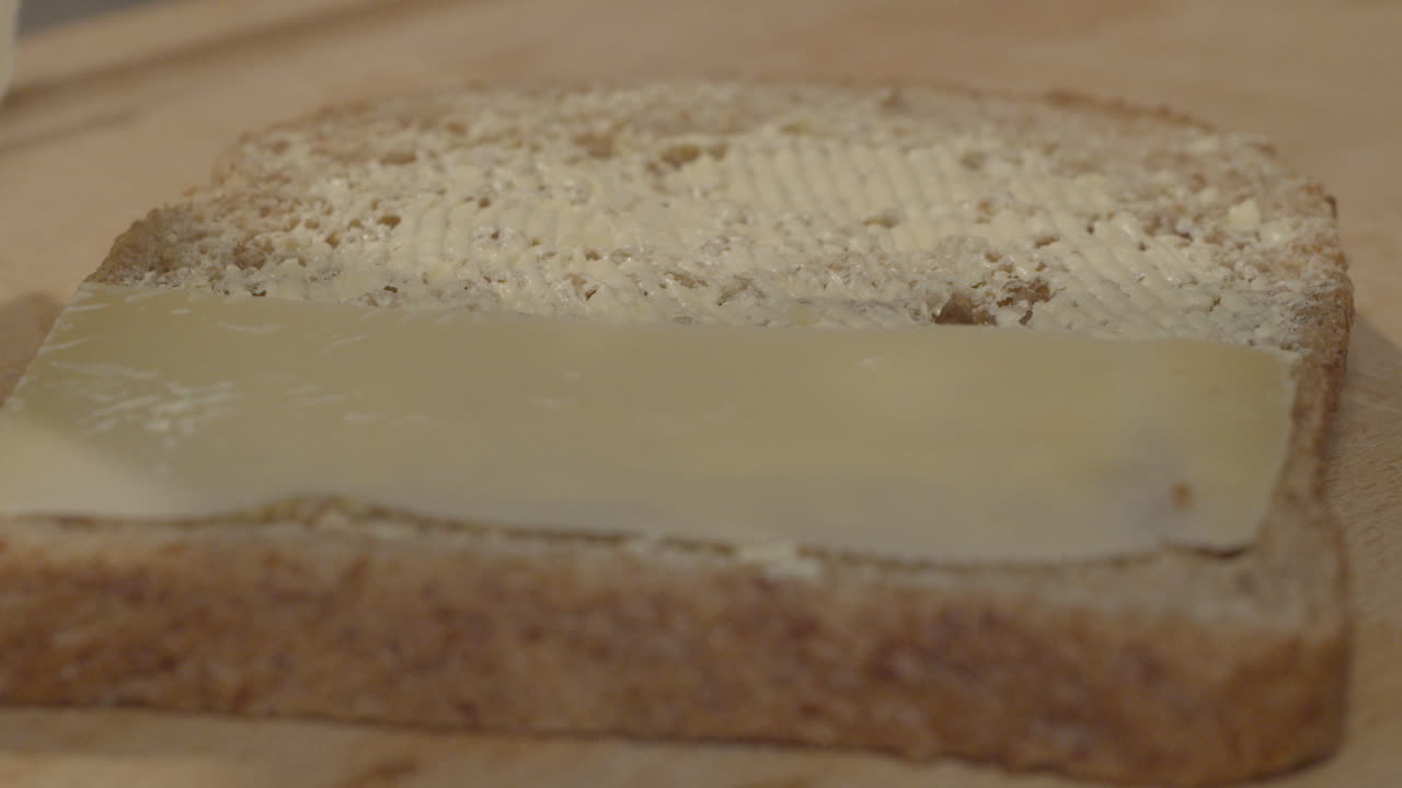 Slices of cheese slowly being put on buttered slice of whole grain bread making a delicious sandwich