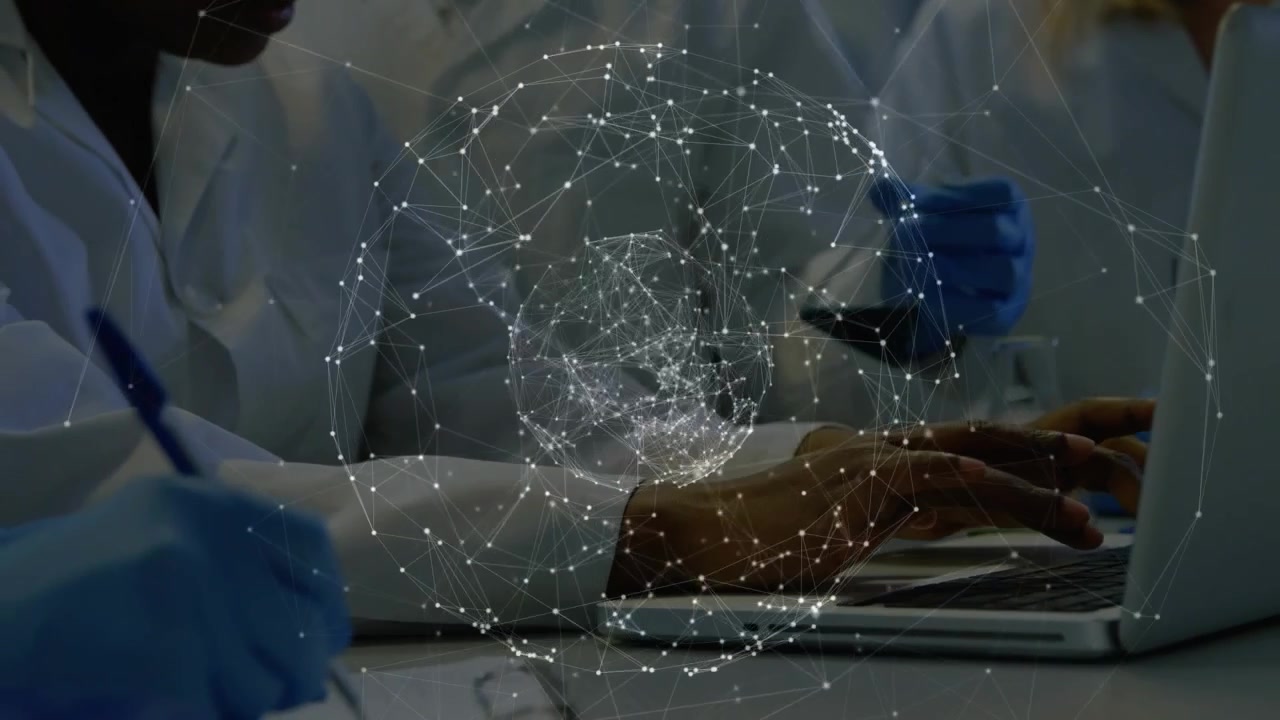 Woman scientist typing laptop driving data sphere while gloved peer handling sample noting lab data
