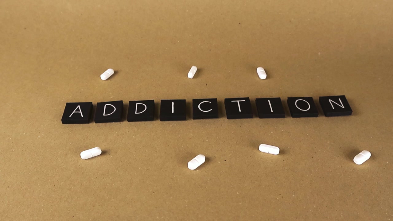 Black letter tiles spelling the word addiction surrounded by white pills, representing the concept of substance abuse, drug dependency, and the dangers of prescription medication overuse