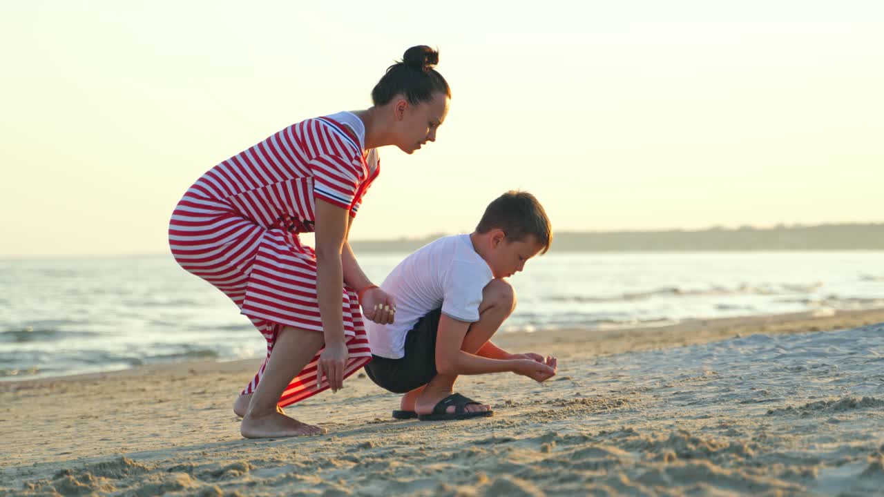 Boy with his mother on a sand beach in the evening. Young woman playing with her son on the beach by the sea.