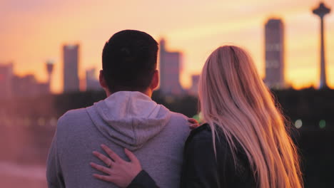 view from the back of a young girl with blond hair hugging an asian guy on the background of the sun